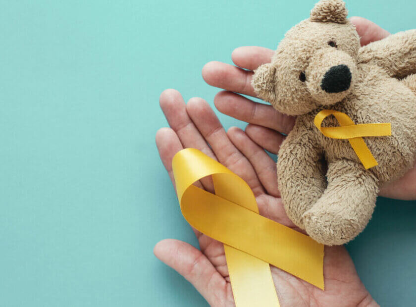 Hands holding children soft toy brown bear with yellow gold ribbon, Childhood cancer awareness